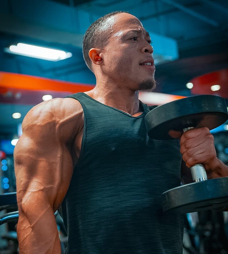 Coach is wearing a sleeveless t-shirt and lifting dumbells